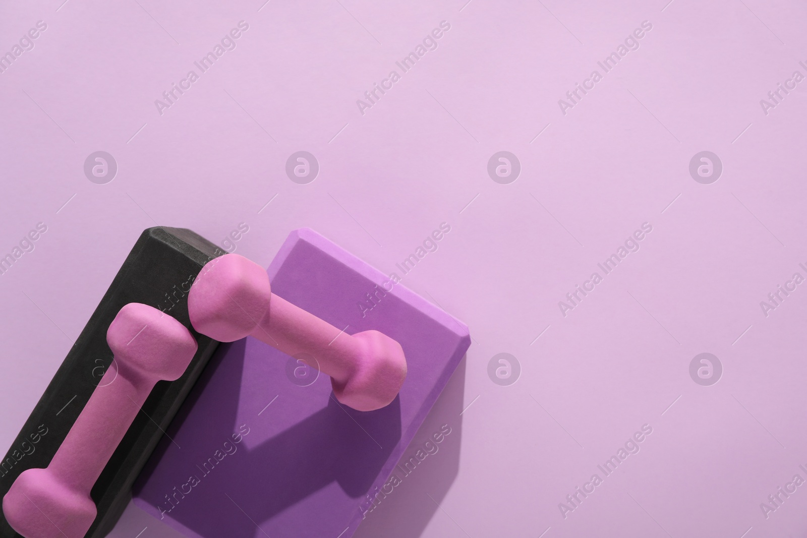 Photo of Two dumbbells and yoga blocks on violet background, flat lay. Space for text