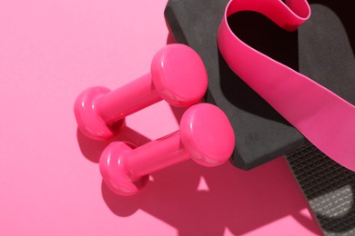 Dumbbells, fitness elastic band and yoga block on pink background, flat lay