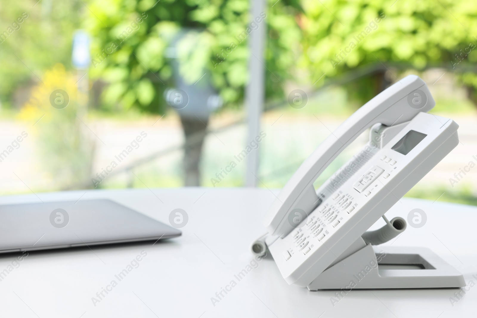 Photo of White telephone and laptop on table indoors. Space for text