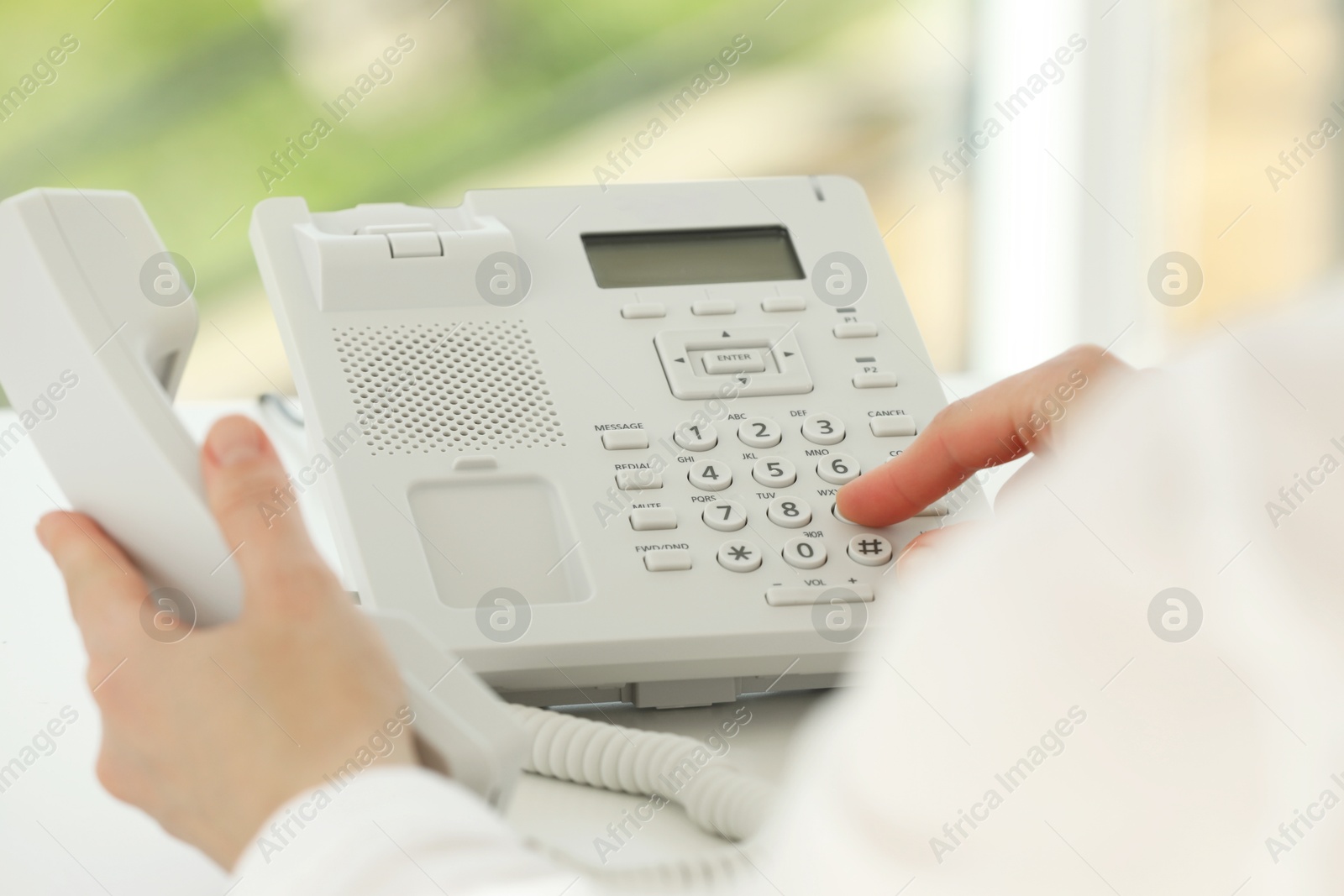 Photo of Assistant dialing number on telephone at white table, closeup