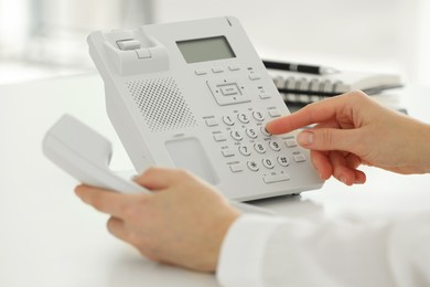 Assistant dialing number on telephone at white table, closeup