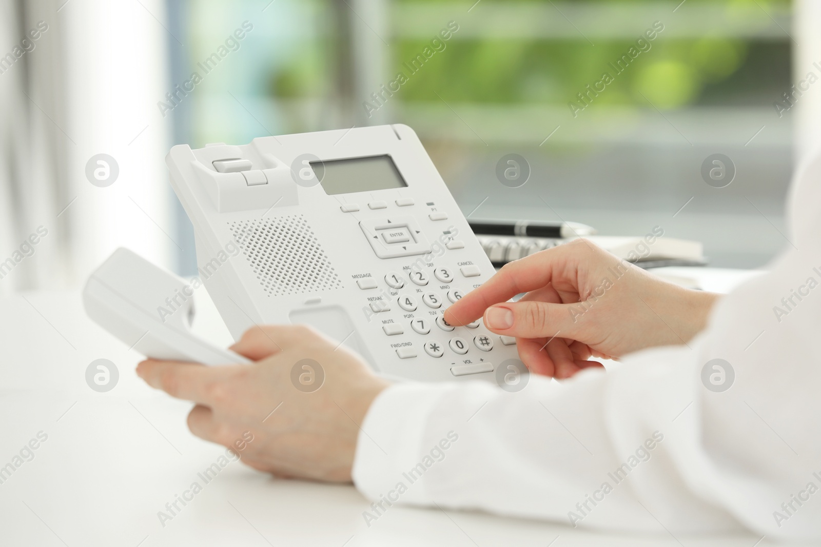 Photo of Assistant dialing number on telephone at white table, closeup