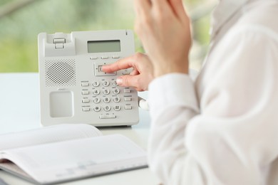 Photo of Assistant dialing number on telephone at table in office, closeup