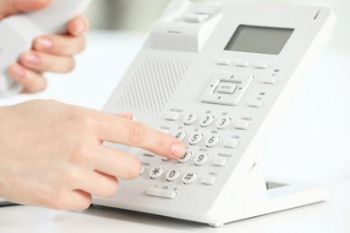 Photo of Assistant dialing number on telephone at white table, closeup