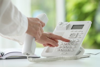 Photo of Assistant dialing number on telephone against blurred background, closeup