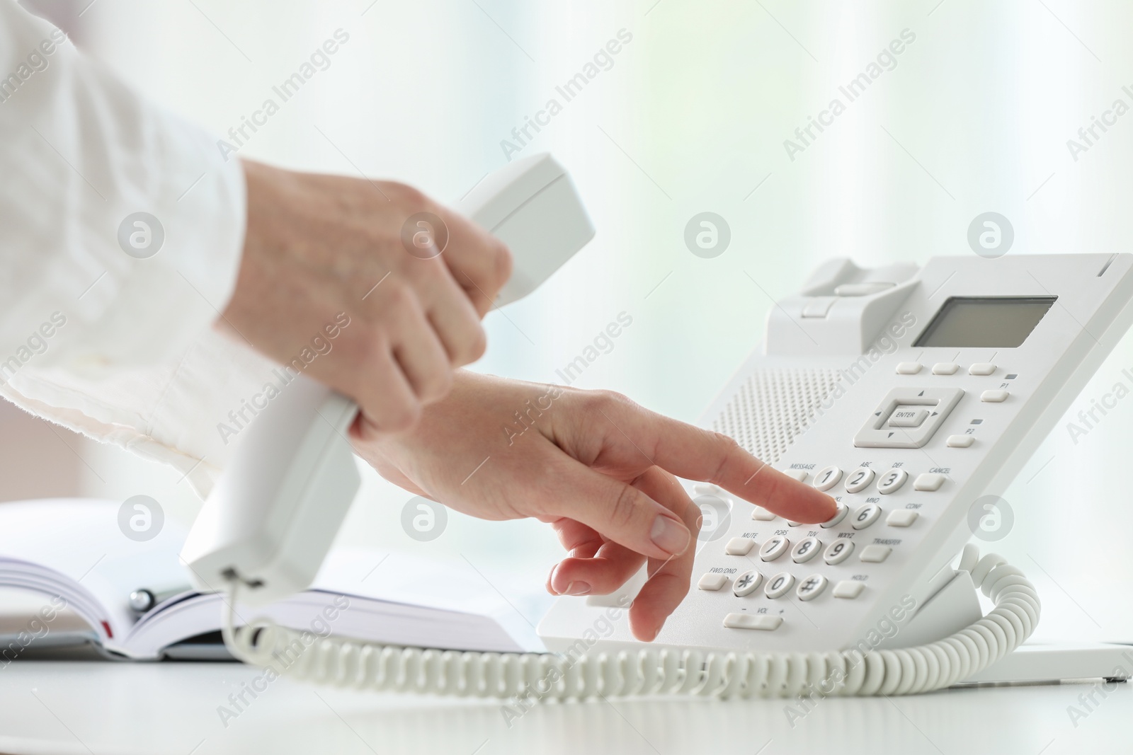 Photo of Assistant dialing number on telephone against blurred background, closeup