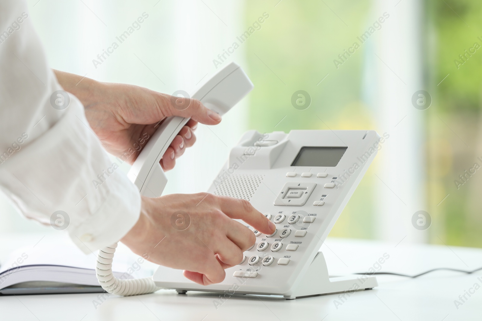 Photo of Assistant dialing number on telephone against blurred background, closeup