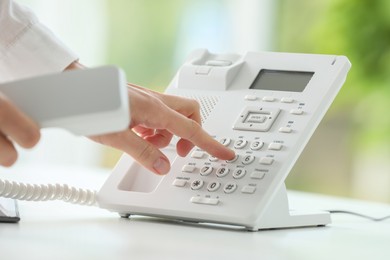 Photo of Assistant dialing number on telephone against blurred background, closeup