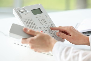 Assistant dialing number on telephone against blurred background, closeup