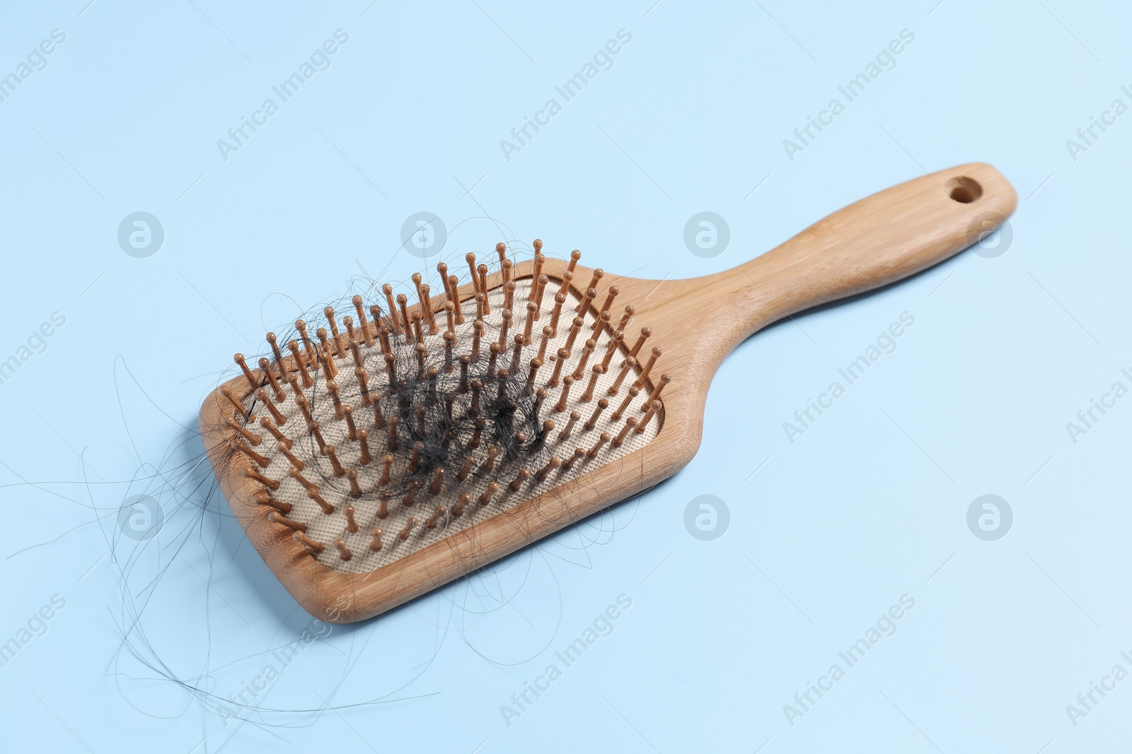 Photo of Wooden brush with lost hair on light blue background