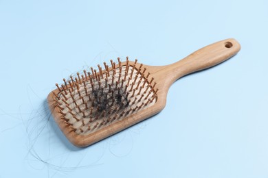 Photo of Wooden brush with lost hair on light blue background