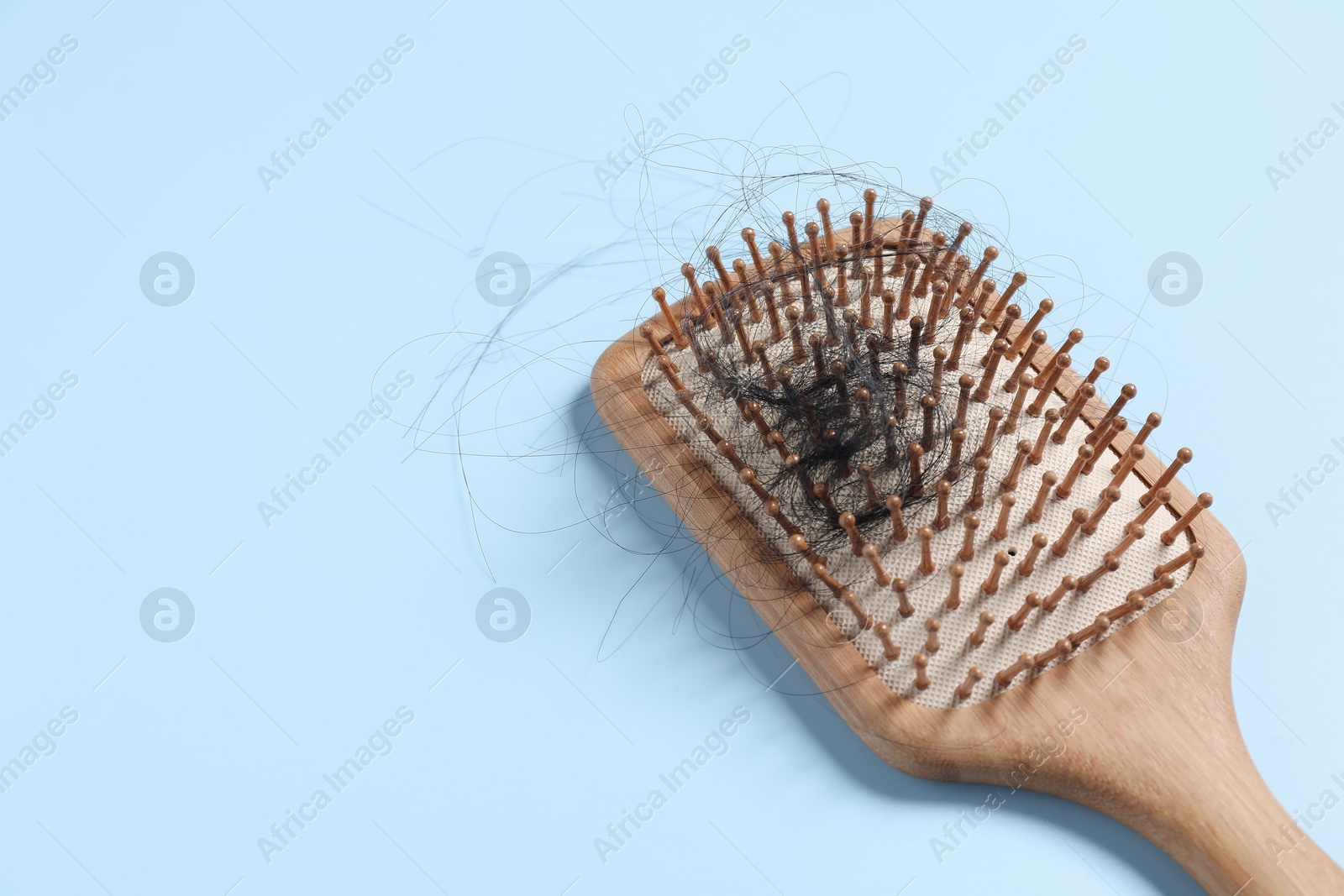 Photo of Wooden brush with lost hair on light blue background, space for text