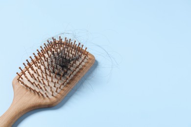 Photo of Wooden brush with lost hair on light blue background, space for text