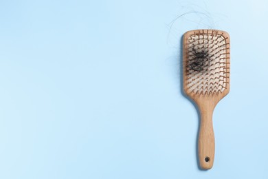 Photo of Wooden brush with lost hair on light blue background, top view. Space for text