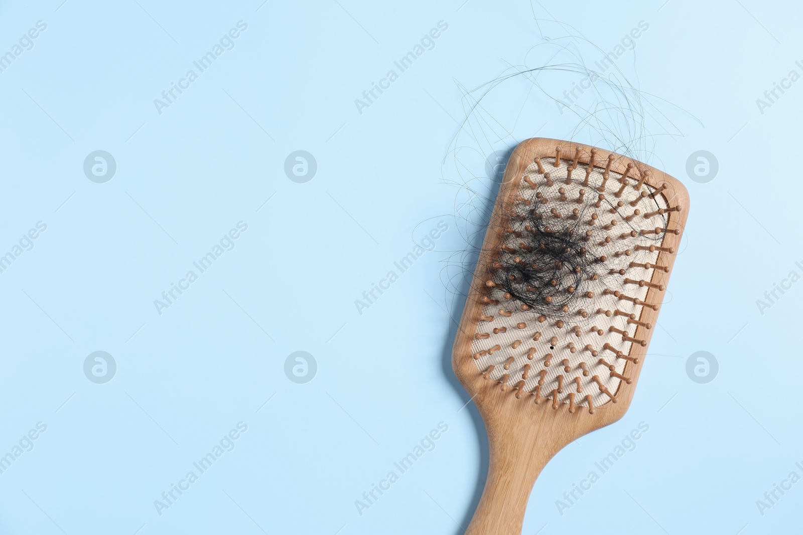 Photo of Wooden brush with lost hair on light blue background, top view. Space for text