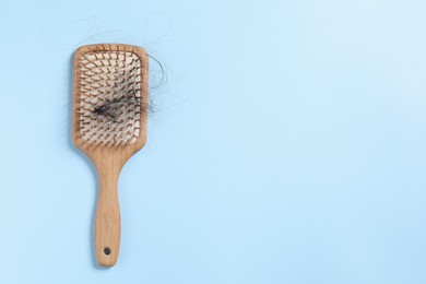 Photo of Wooden brush with lost hair on light blue background, top view. Space for text