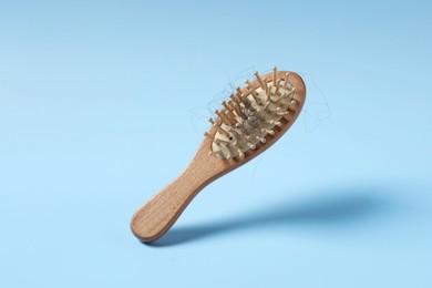 Photo of Wooden brush with lost hair in air on light blue background