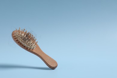 Photo of Wooden brush with lost hair in air on light blue background, space for text