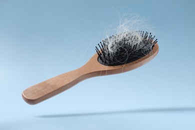 Photo of Wooden brush with lost hair in air on light blue background