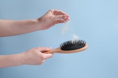 Photo of Woman taking her lost hair from brush on light blue background, closeup