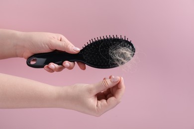 Photo of Woman taking her lost hair from brush on pink background, closeup