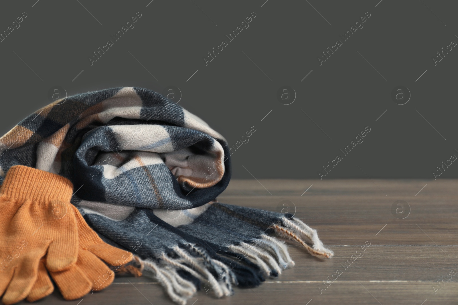 Photo of Soft checkered scarf and gloves on wooden table against gray background, space for text