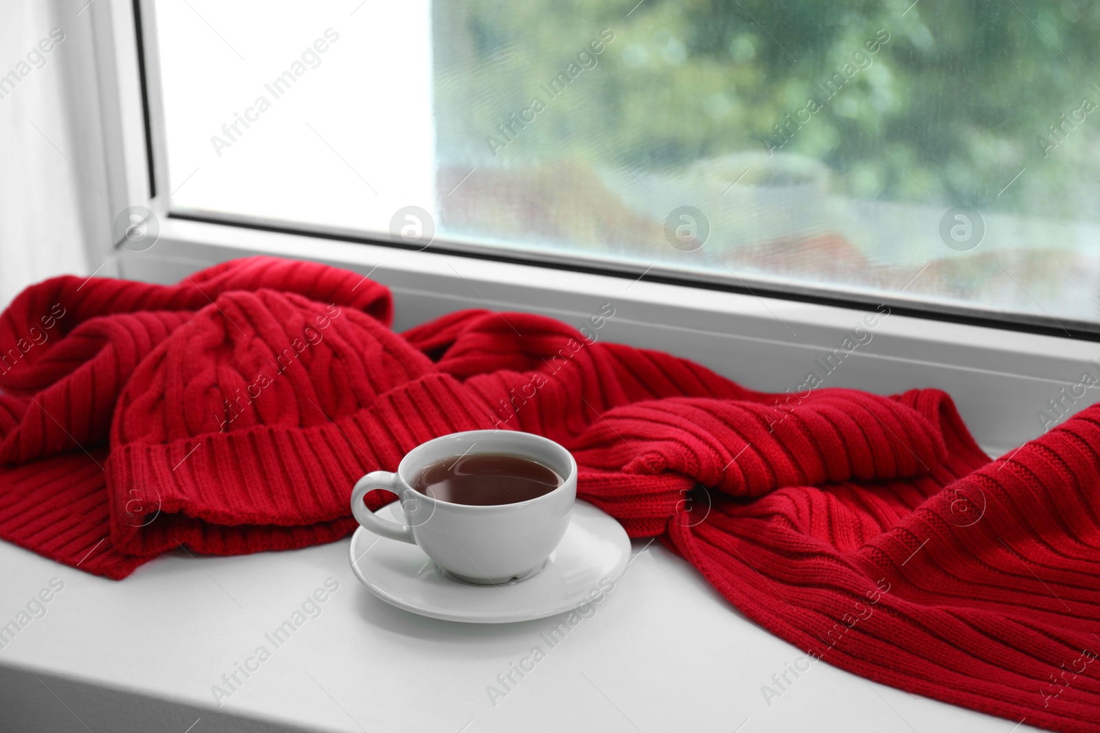 Photo of Red knitted scarf, hat, tea on windowsill