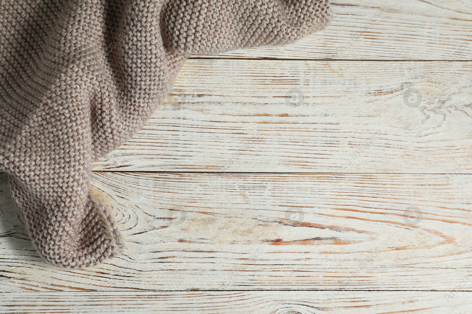 Photo of Gray knitted scarf on white wooden table, top view. Space for text