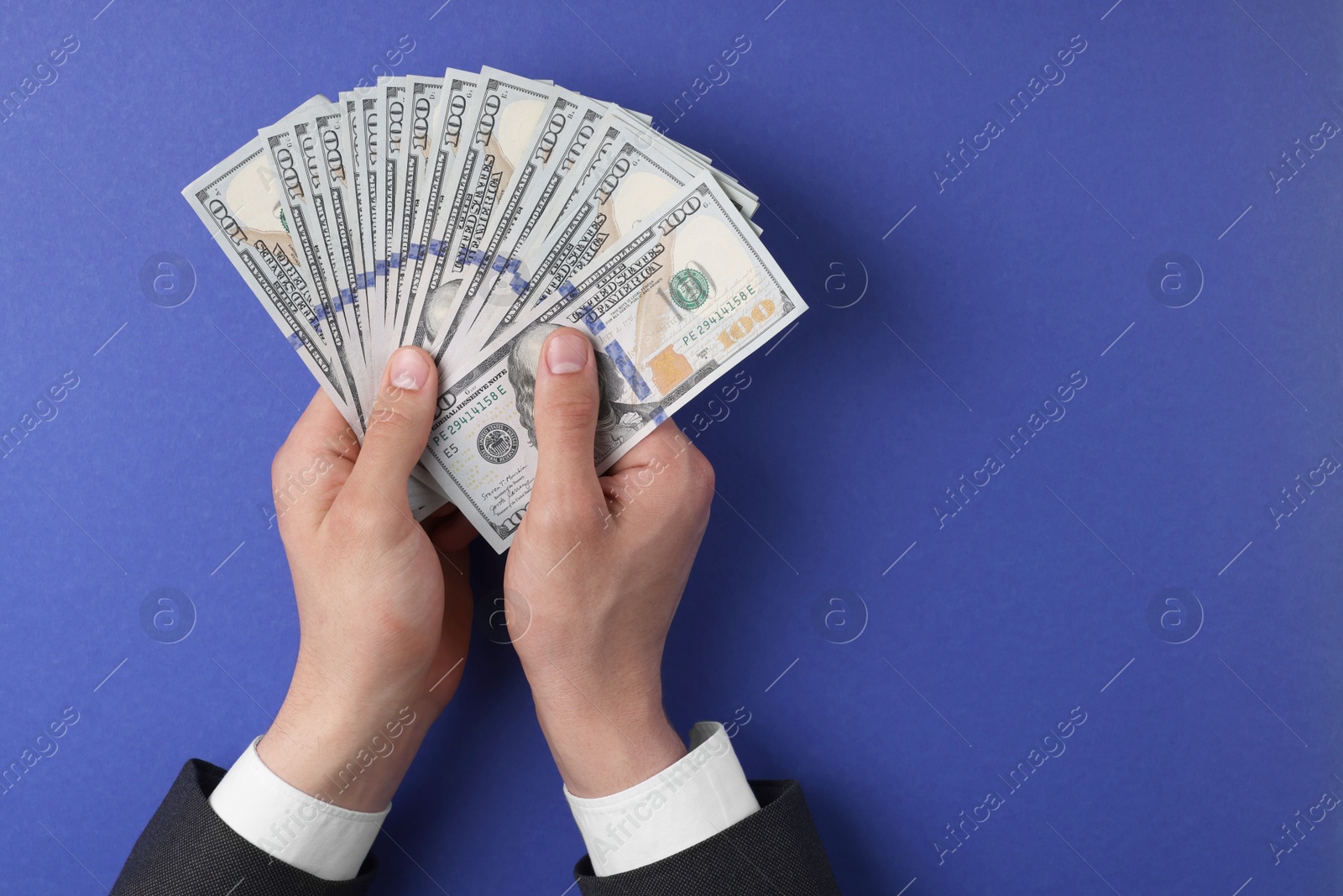 Photo of Money exchange. Man holding dollar banknotes on blue background, top view