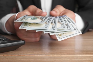 Photo of Money exchange. Man counting dollar banknotes at wooden table, closeup