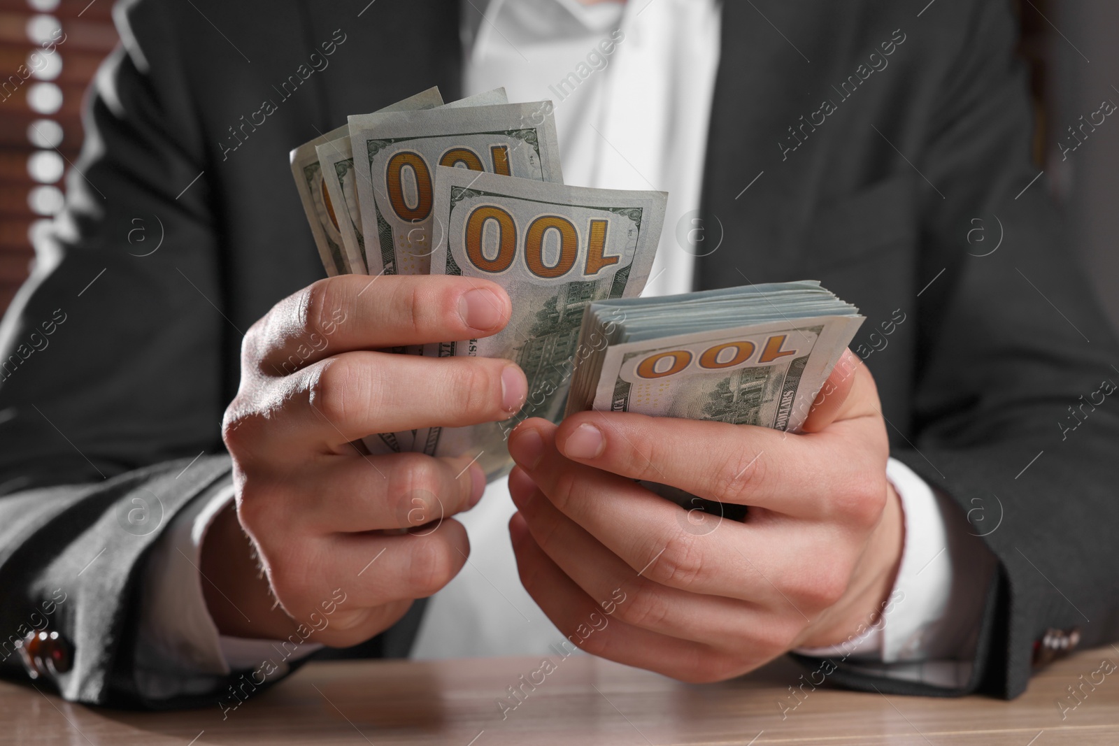 Photo of Money exchange. Man counting dollar banknotes at wooden table, closeup