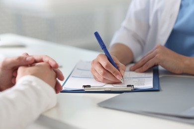 Professional doctor working with patient at white table in hospital, closeup