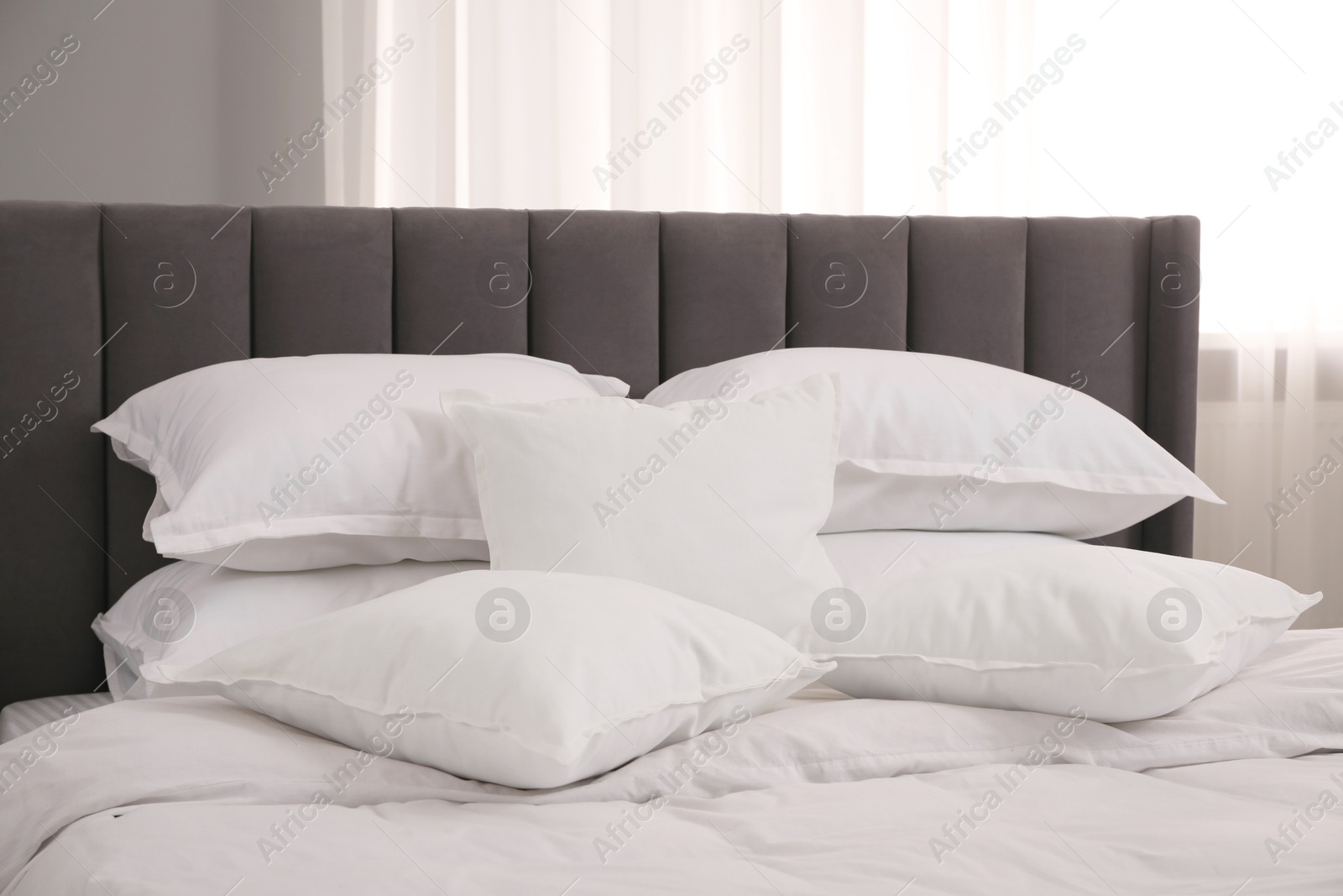 Photo of Many soft white pillows and duvet on bed indoors