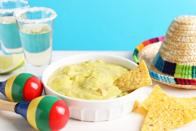 Delicious guacamole with nachos chips, Mexican sombrero hat, maracas and tequila on white wooden table