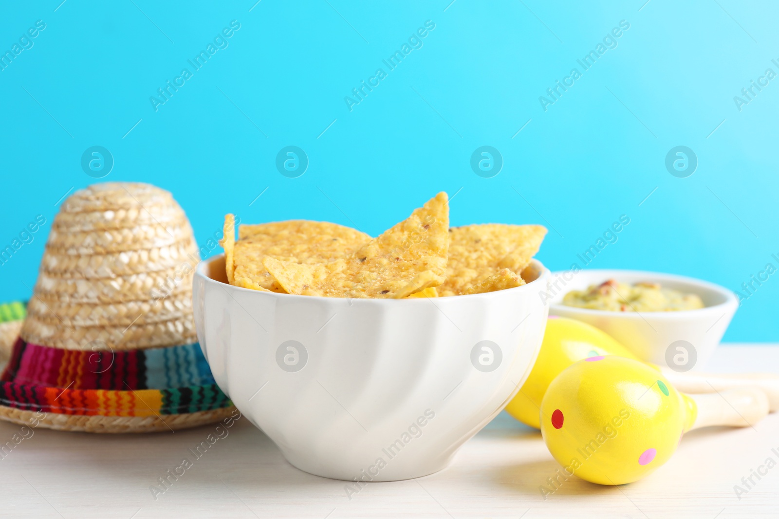 Photo of Mexican sombrero hat, nachos chips, guacamole and maracas on white wooden table