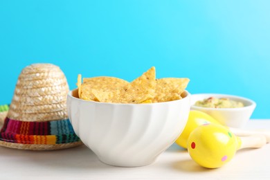 Mexican sombrero hat, nachos chips, guacamole and maracas on white wooden table