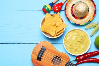 Delicious guacamole with nachos chips, Mexican sombrero hat, ukulele and maracas on light blue wooden table, flat lay. Space for text