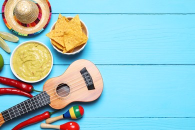 Delicious guacamole with nachos chips, Mexican sombrero hat, ukulele and maracas on light blue wooden table, flat lay. Space for text