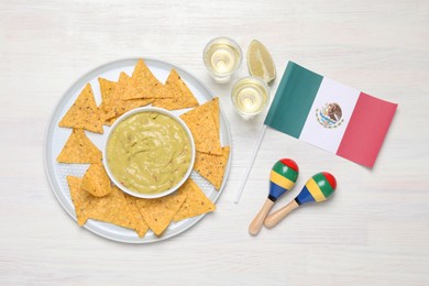 Mexican flag, maracas, tequila, nachos chips and guacamole on white wooden table, flat lay