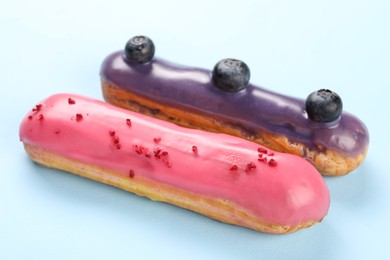 Photo of Delicious eclairs covered with glaze on light blue background, closeup