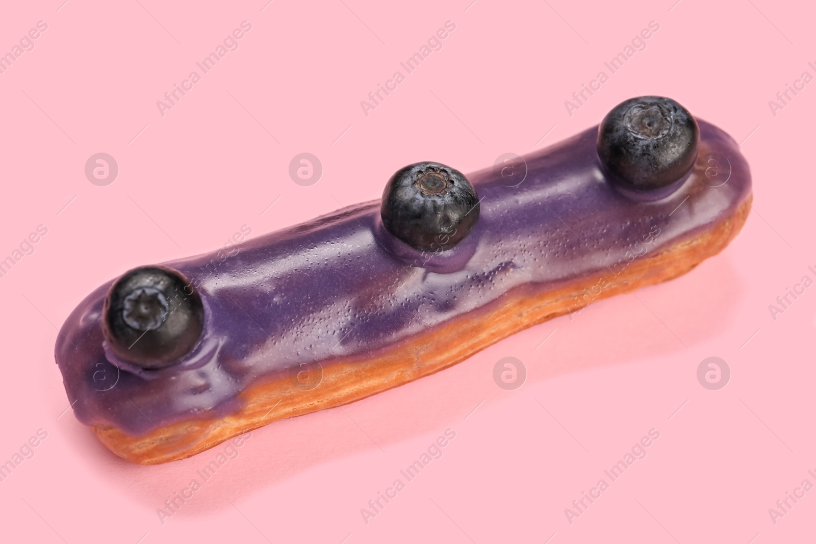 Photo of Delicious eclair decorated with blueberries on pink background