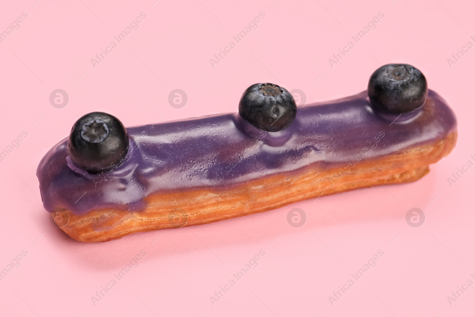 Photo of Delicious eclair decorated with blueberries on pink background