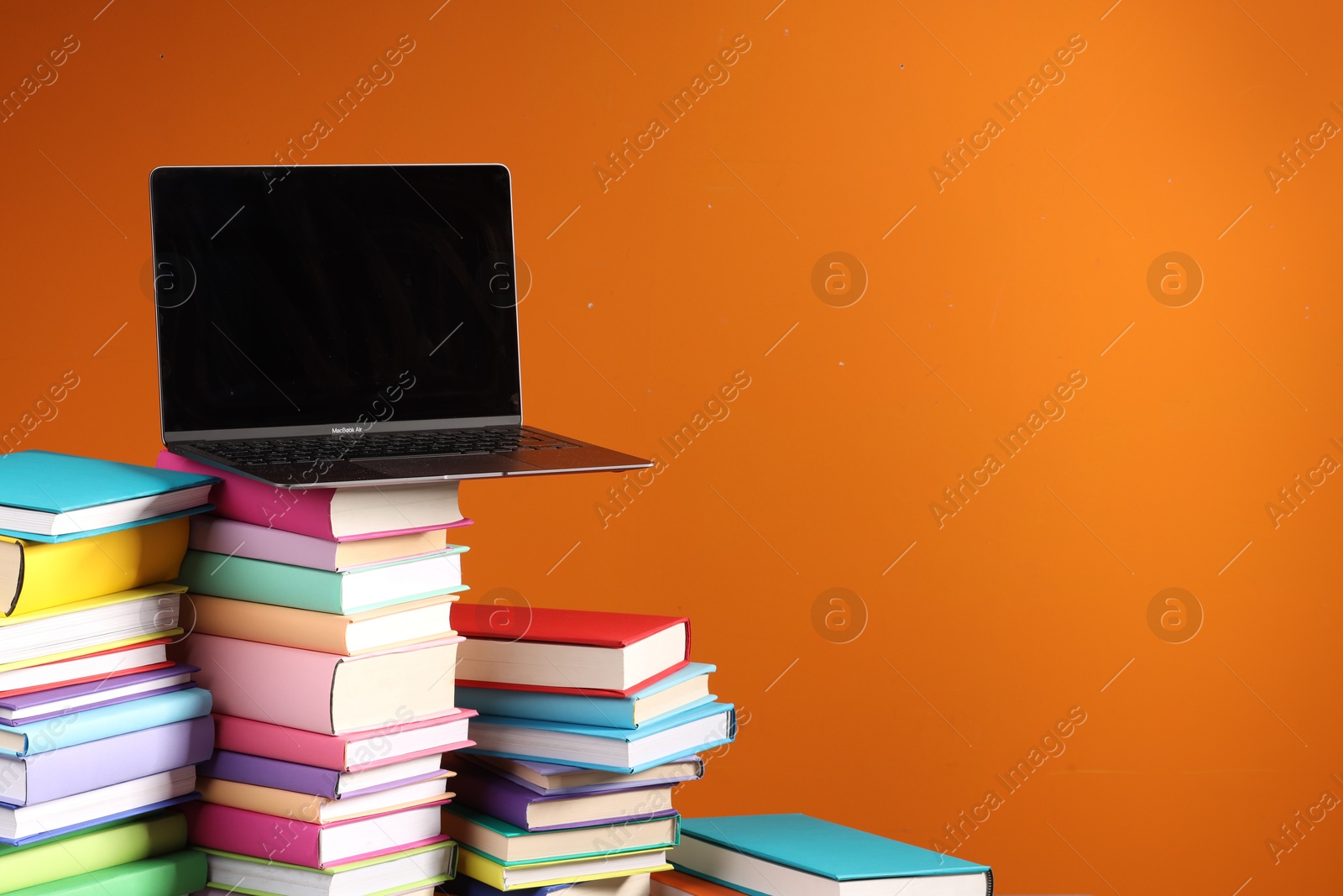 Photo of Stacks of colorful books and laptop on orange background, space for text