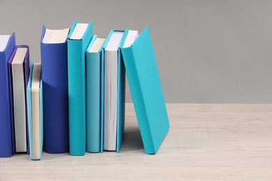 Many colorful books on white wooden table against light grey background, space for text