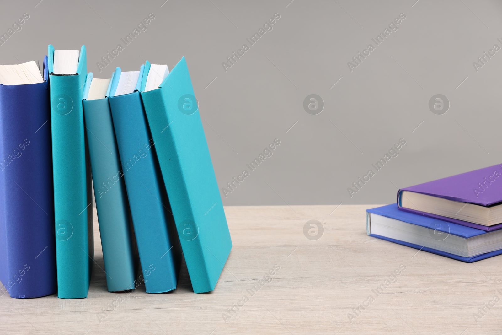 Photo of Many colorful books on white wooden table against light grey background