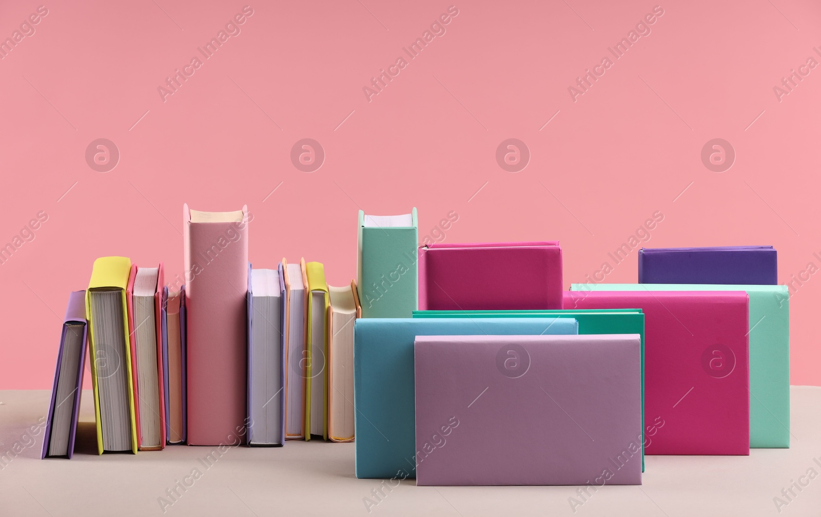 Photo of Many colorful books on beige table against pink background, space for text