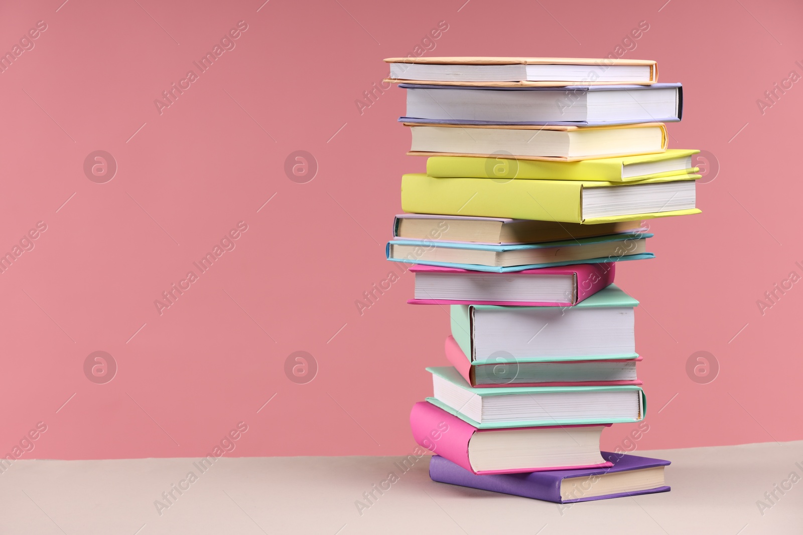 Photo of Stack of colorful books on beige table against pink background, space for text