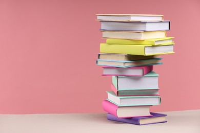 Photo of Stack of colorful books on beige table against pink background, space for text