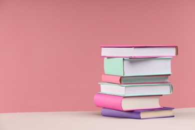 Photo of Stack of colorful books on beige table against pink background, space for text