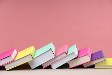 Photo of Many colorful books on beige table against pink background, space for text